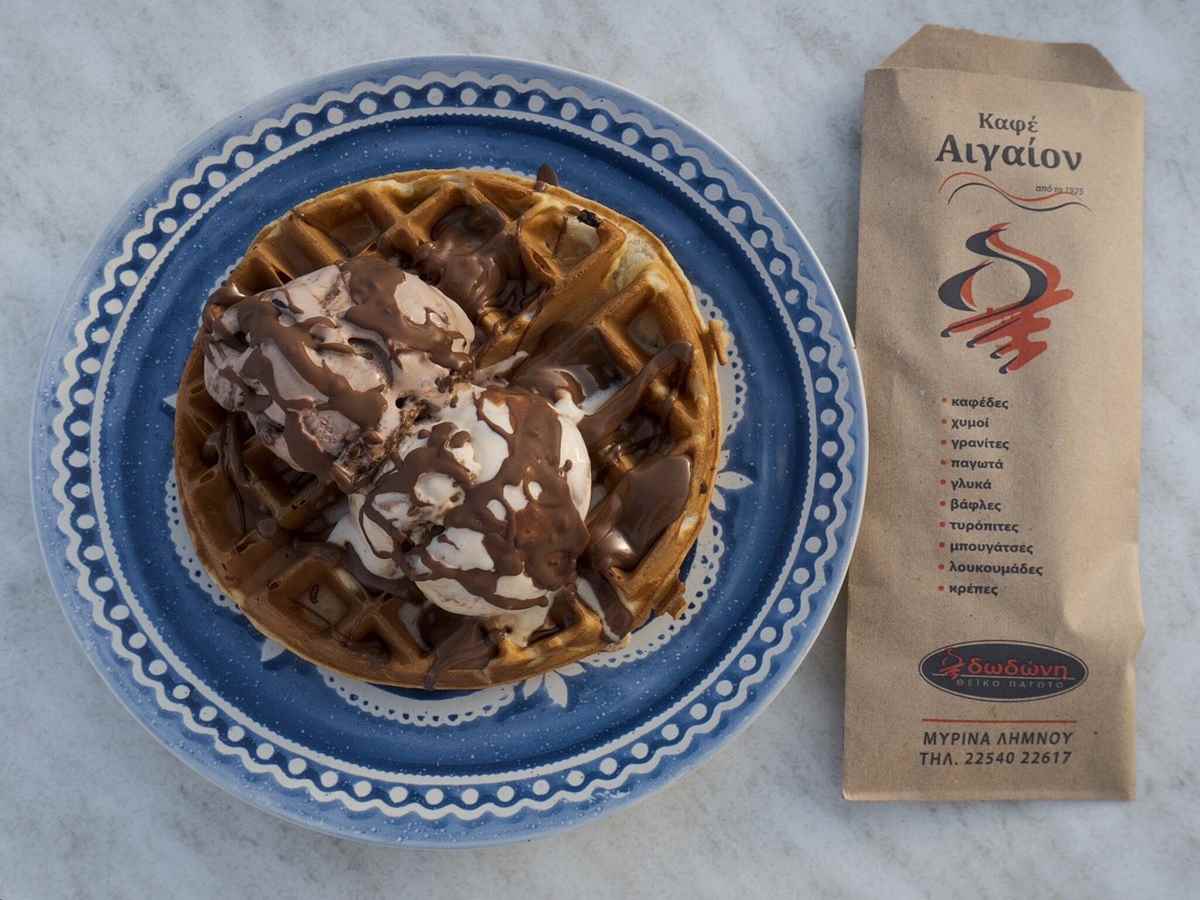 a waffle with ice cream and chocolate sauce on a blue and white plate